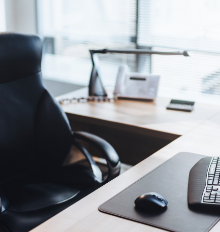 A clean, modern office desk with a black chair, computer keyboard, mouse, desk lamp, and notepad, suggesting a professional work environment.